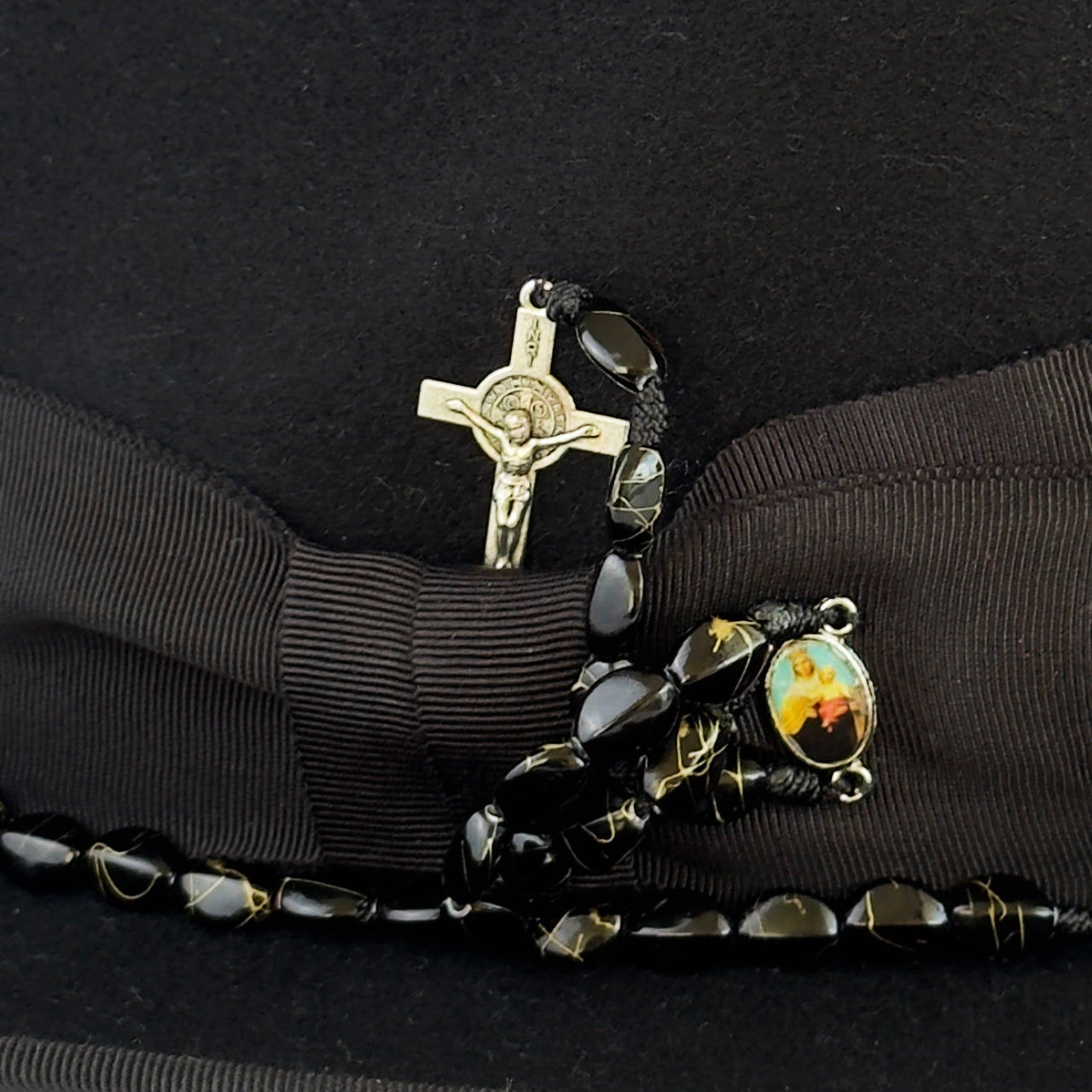 Detalle artesanal de GOYO con crucifijo, cuentas y medalla